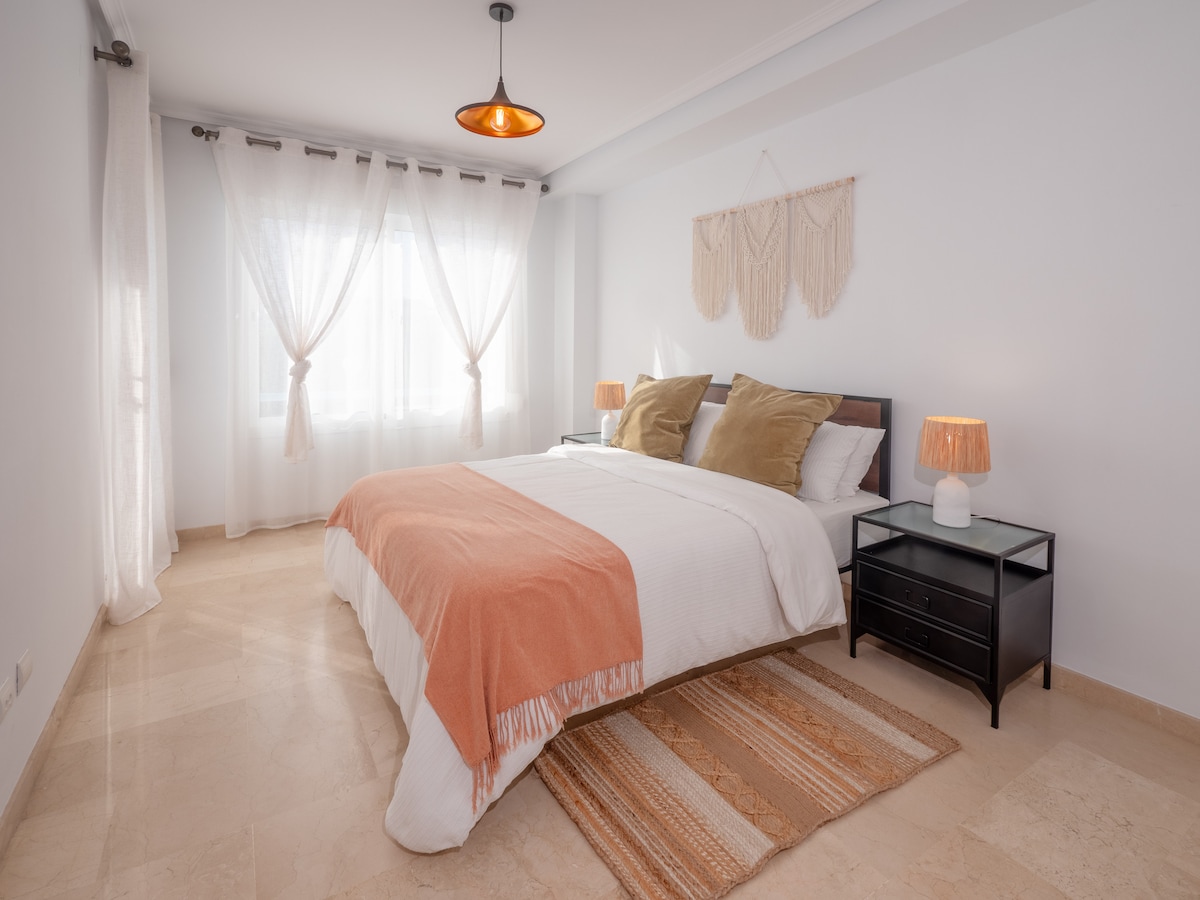 חדר השינה הראשי מואר ומזמין, עם מיטת קינג סייז עם מצעים רכים, שולחנות ליד המיטה ועיצוב מסוגנן. מקום מרגיע ללילות נינוחים.