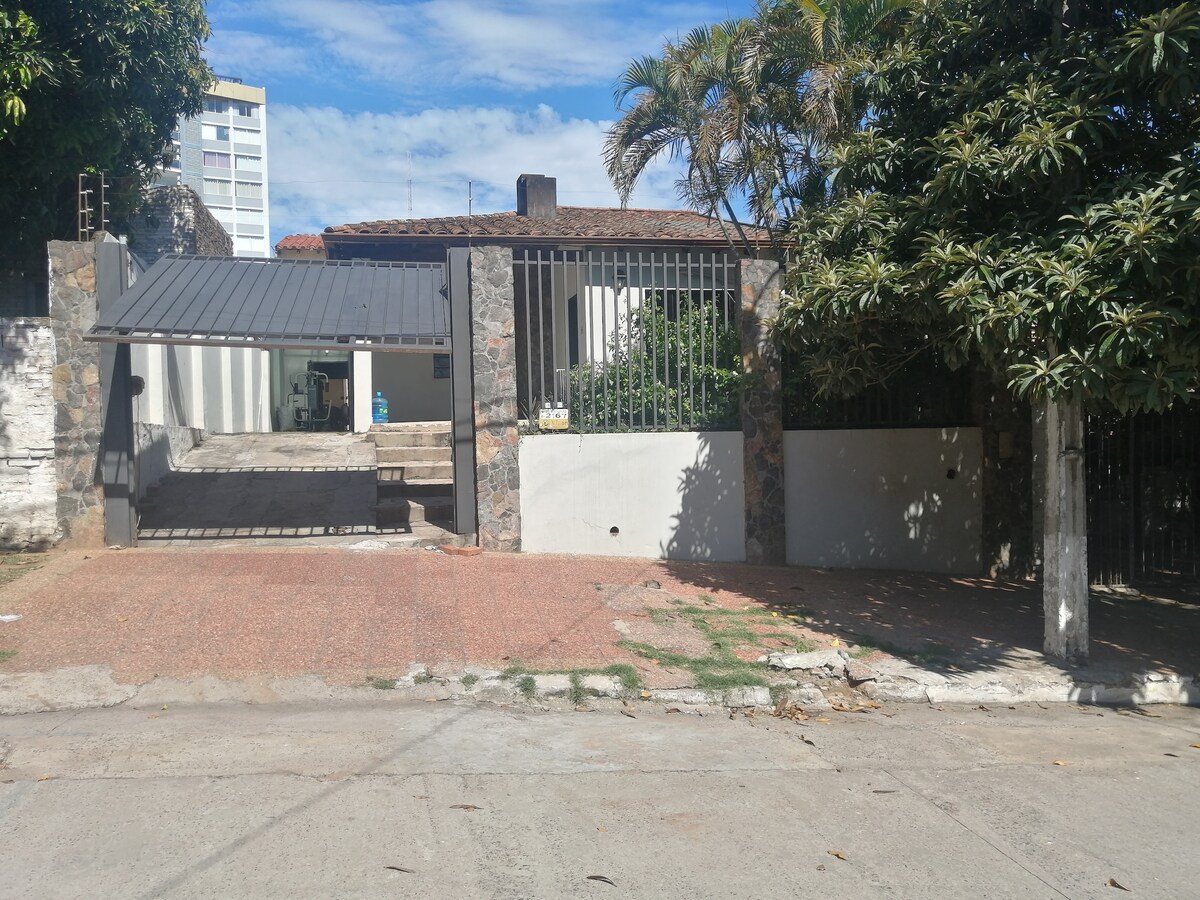 The exterior of the property features a stone wall and a gated entrance, providing a sense of privacy. A spacious driveway leads to the entrance, while lush greenery and palm trees enhance the welcoming vibe of the outdoor area.