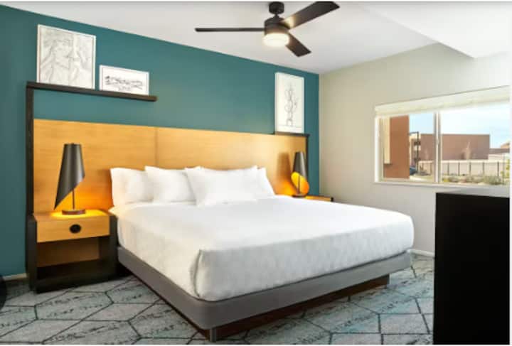 Dhomë gjumi e ndritshme dhe me stil, me një krevat dopio "king" me një kokë krevati moderne me panele druri, komodina elegante pranë krevatit dhe ndriçim të ngrohtë dekorativ. Një mur me ngjyrë të kaltër të gjelbër i jep një prekje të gjallë, ndërsa dritaret e mëdha ofrojnë dritë natyrale. Përfshin një suitë private