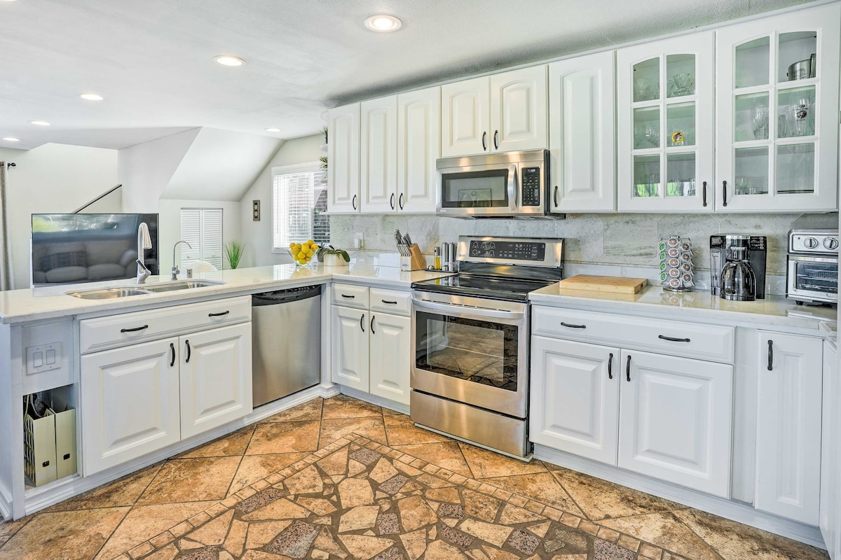 The spacious kitchen features white cabinetry with glass accents, stainless steel appliances including an oven and microwave, and a central island with a wooden cutting board. Natural light brightens the room, complemented by a patterned tile floor.