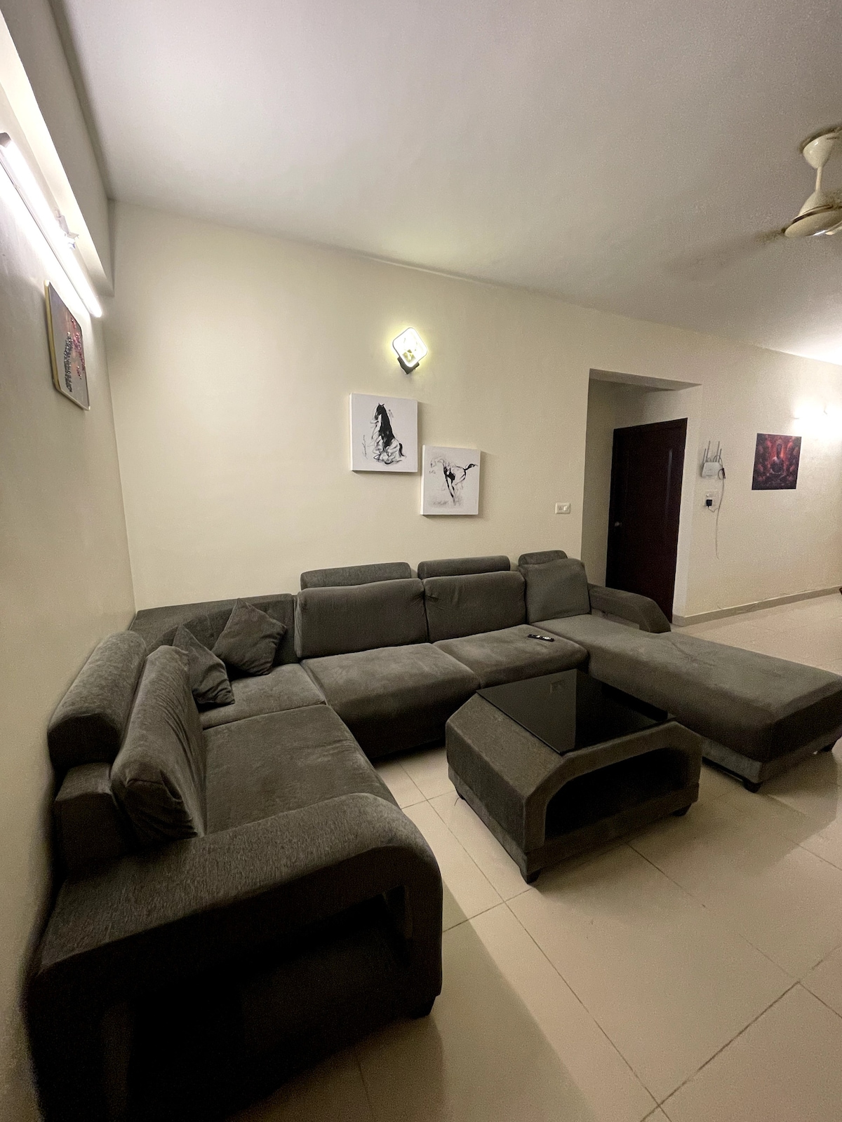 A spacious living area is featured, showcasing a contemporary gray sectional sofa arranged for comfort. A sleek glass coffee table sits in front of the seating area, complemented by simple wall art. Soft lighting enhances the room's welcoming atmosphere.