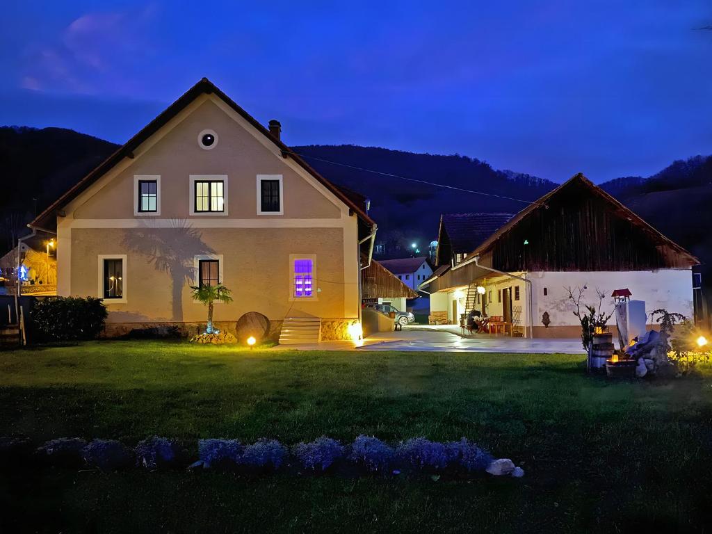 The villa's exterior is illuminated at dusk, showcasing a combination of traditional and modern architecture. The well-maintained lawn features soft lighting, enhancing the inviting appearance of the building and surrounding landscape. The backdrop of rolling hills adds a serene atmosphere to the setting.