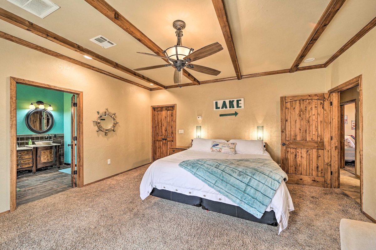 A spacious primary bedroom features a king bed with a light blue throw blanket, accompanied by wood beam ceilings. Two wooden doors lead to separate areas, while a round mirror and stylish lighting enhance the room's design. Soft carpet covers the floor, adding comfort.