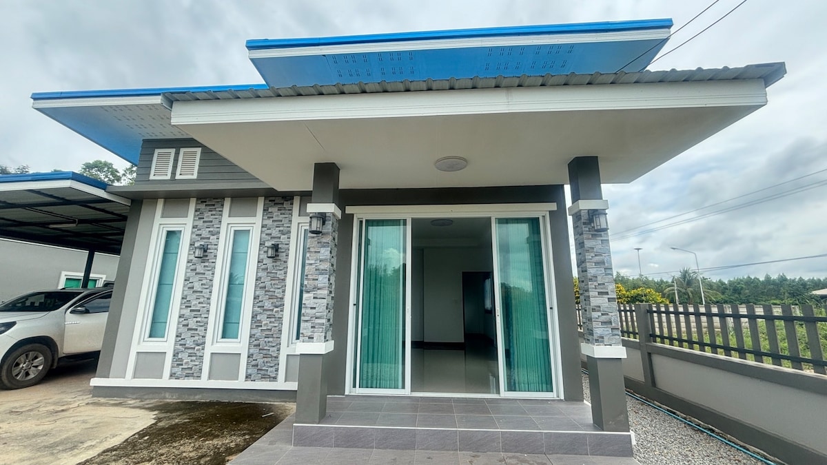 A modern exterior view of the property is showcased, featuring a covered entrance with large glass doors. The facade is complemented by stone detailing and a blue overhang, while a gravel pathway extends toward the driveway.