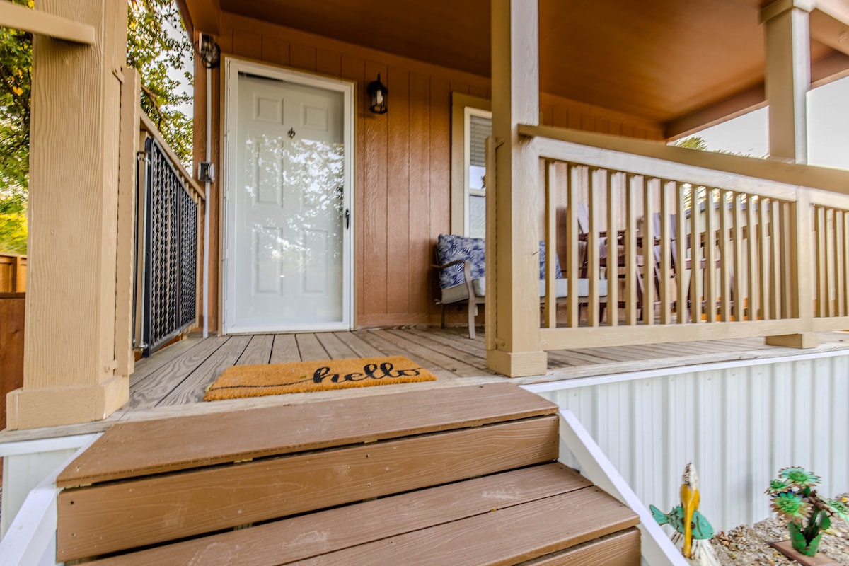 A welcoming entrance is showcased with a set of sturdy wooden steps leading up to a porch. A door featuring a clear window provides access, while a doormat with the word 'hello' greets visitors. The porch is surrounded by wooden railings and comfortable seating.