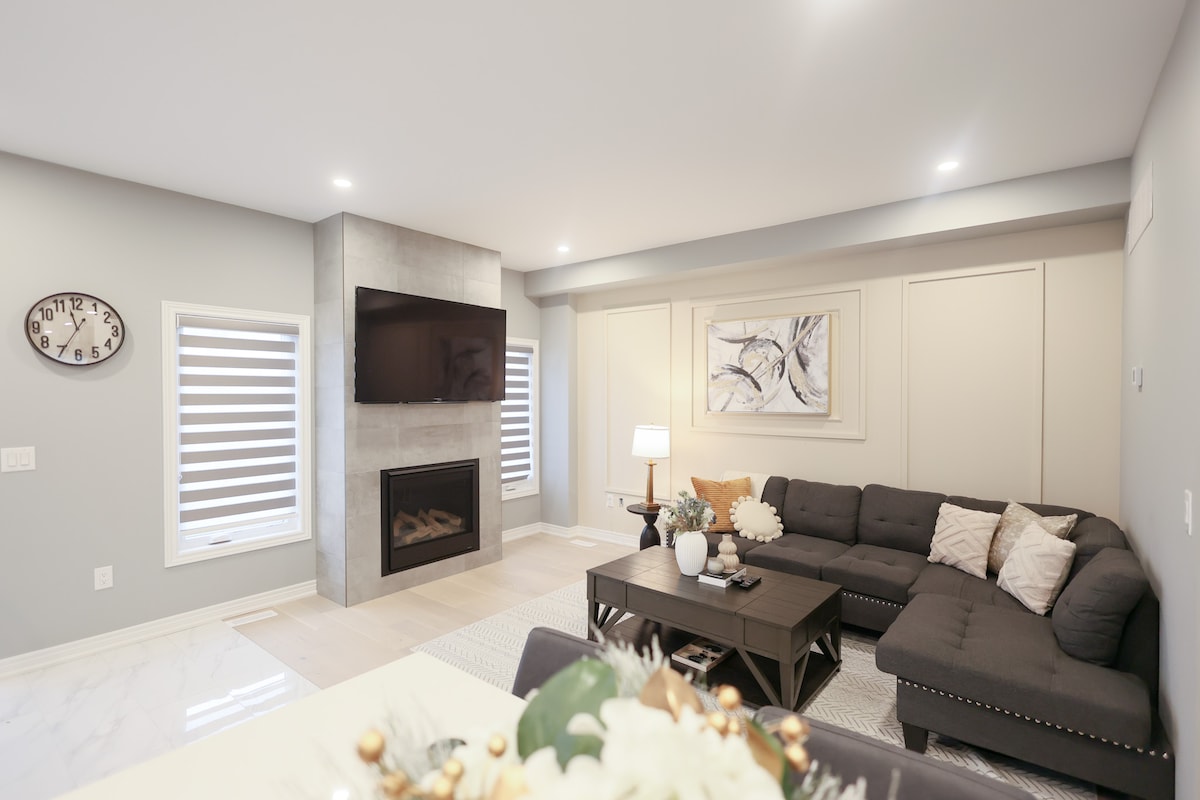 Elegante sala de estar con un acogedor sofá, TV montada en la pared, chimenea moderna, arte abstracto, elegante mesa de café, iluminación suave y elegantes persianas.