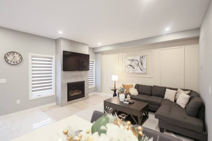 סלון אופנתי הכולל ספה נפתחת נוחה, טלוויזיה המותקנת על הקיר, אח מודרנית, אמנות אבסטרקטית, שולחן קפה אלגנטי, תאורה רכה ותריסים אופנתיים.