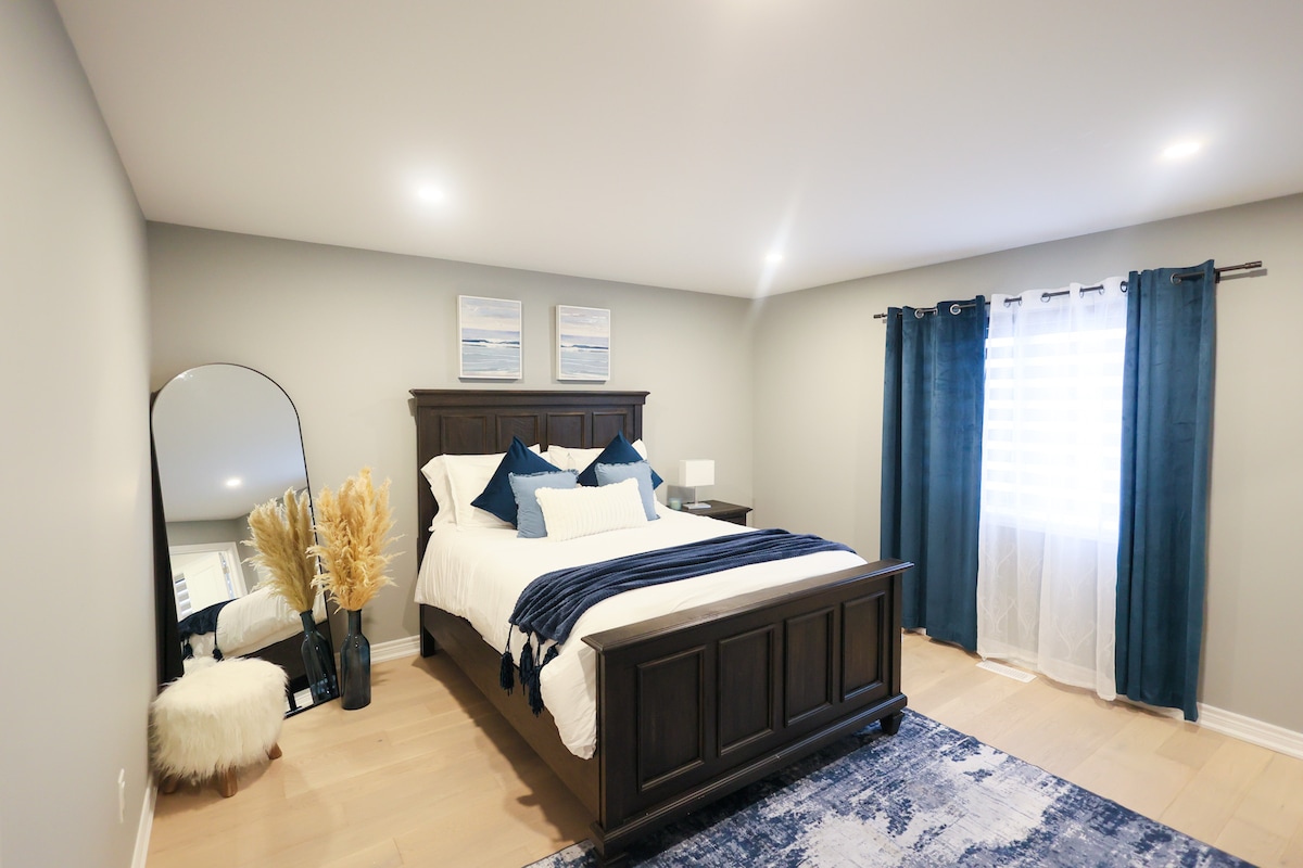 Amplio dormitorio con una cama de madera resistente, almohadas suaves, una manta acogedora, un espejo de pie elegante, una decoración elegante de hierba de las pampas, un taburete mullido, una alfombra vibrante y una gran ventana.