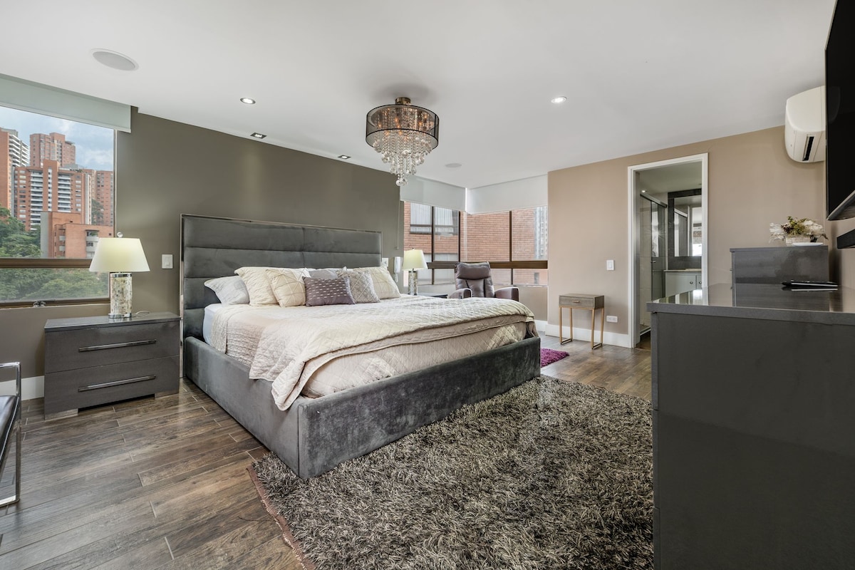 Glavna spavaća soba uključuje veliki bračni krevet s uzglavljem, lusterom i ukrasnom rasvjetom.