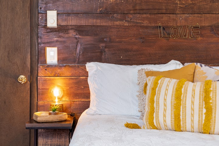 Cozy bedroom corner with warm rustic wood accents, soft lighting, and cheerful yellow details. A charming space designed for comfort, relaxation, and a little extra love in every stay.