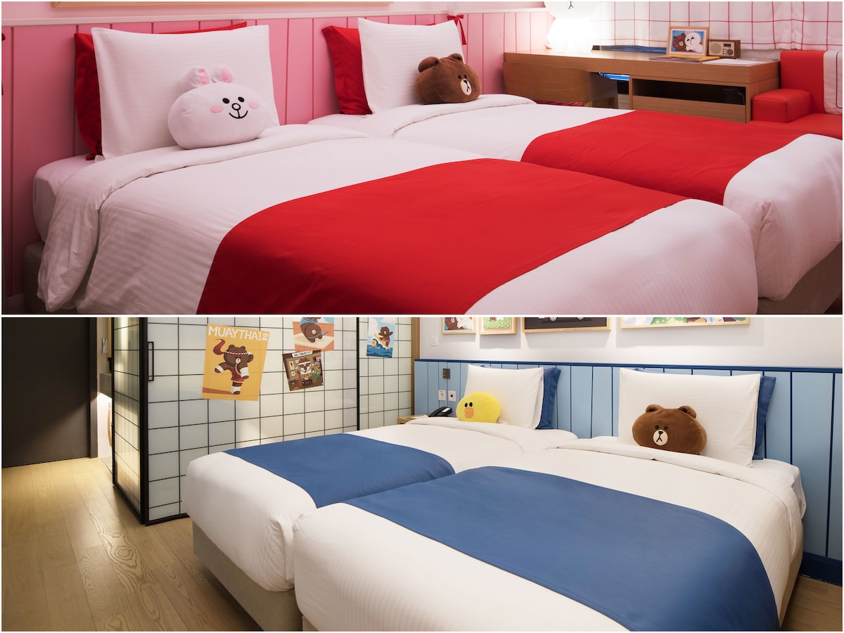 Two separate sleeping areas are displayed, each featuring spacious beds with playful themed bedding. The upper section is adorned with bright red accents, while the lower section exhibits calming blue tones. Plush character pillows, designed as popular figures, enhance the cheerful atmosphere.