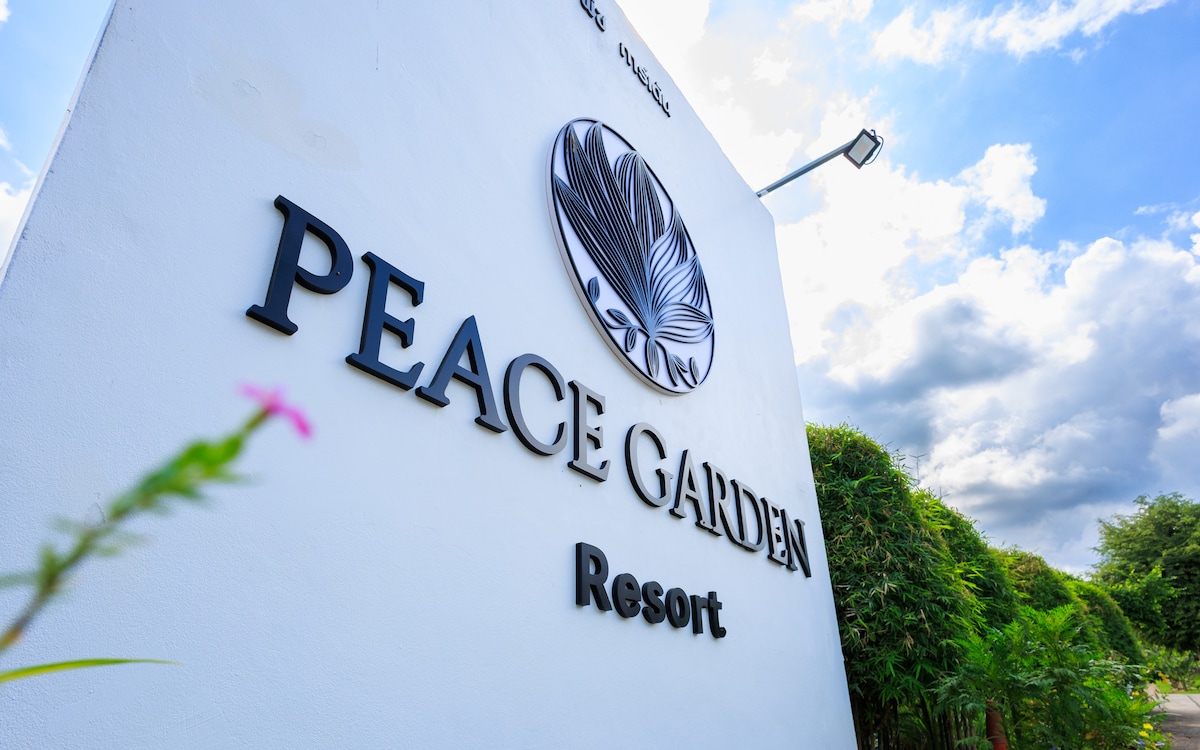 The entrance signage of Peace Garden Resort is prominently displayed against a clear blue sky, featuring the resort's name in bold letters. Surrounding greenery is visible, enhancing the welcoming atmosphere of the resort.