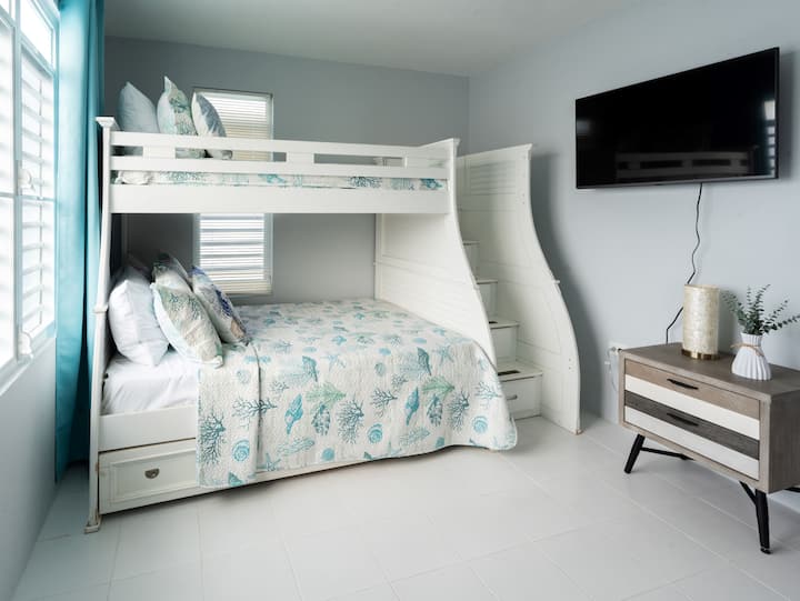 Segundo dormitorio con una litera (tamaño individual en la parte superior, tamaño completo en el centro y un tamaño individual extraíble en la parte inferior), amplios cajones, un televisor de 43pulgadas, un armario y un baño adjunto.