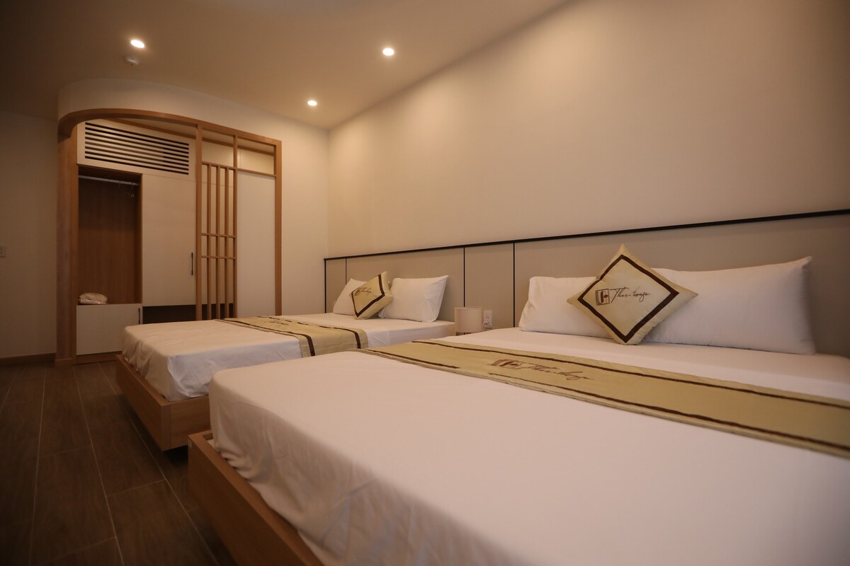 The room features two spacious beds with neutral bedding, accented by decorative pillows. A wooden partition separates the sleeping area from a closet space. Soft lighting illuminates the area, creating a calming environment.