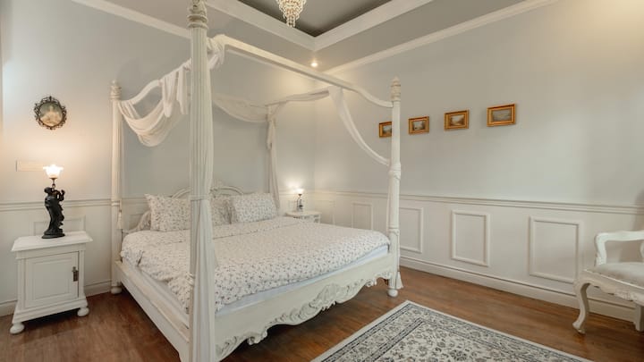 An elegant room with a classic four-poster bed, soft floral accents, and vintage charm, complemented by an ensuite bathroom for a relaxing and refined stay.