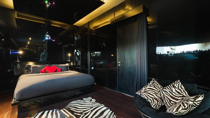 A bold and stylish room with sleek black walls, ambient lighting, and eclectic zebra-print accents, creating a dramatic and modern atmosphere perfect for a unique getaway.