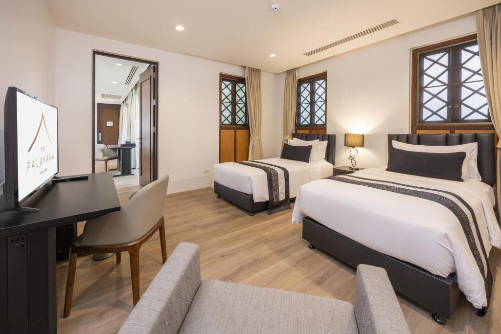 A bright and spacious room features two well-appointed beds, one King and one Twin. A modern television is positioned on a sleek desk beside a comfortable chair. Natural light enters through two patterned windows, while neutral tones create an inviting atmosphere.
