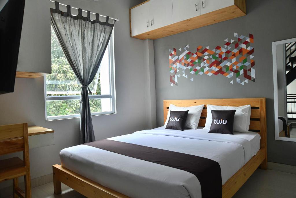 A double room features a spacious bed with two decorative pillows. A geometric wall design adds visual interest. Natural light filters through a curtain-draped window. A wooden table and a flat-screen TV are present, enhancing the functionality of the space.