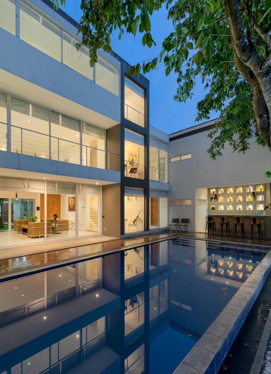 A modern villa is reflected in the tranquil pool, showcasing sleek architecture with large windows. The inviting outdoor space is framed by greenery, while soft lighting highlights the contemporary design, creating a serene and connected atmosphere between the indoor and outdoor areas.