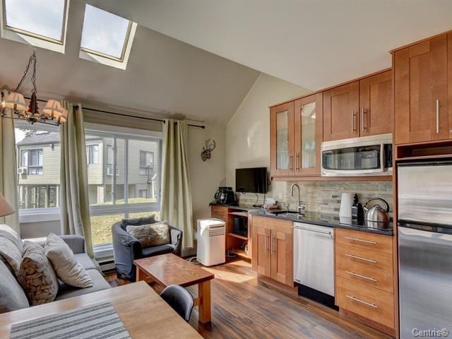 A well-equipped kitchenette is visible, featuring wooden cabinetry and modern appliances, including a microwave and stovetop. Sunlight fills the open living area through large skylights and a window, accentuating the comfortable seating arrangement and natural wood flooring.