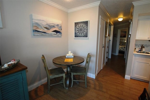 A round wooden table with two matching chairs is positioned against a light gray wall. Above the table, artwork depicting abstract ocean waves adds a calming touch. A small decorative tray with items rests on the table, while a glimpse of the hallway leading to the bedroom can be seen in the background.