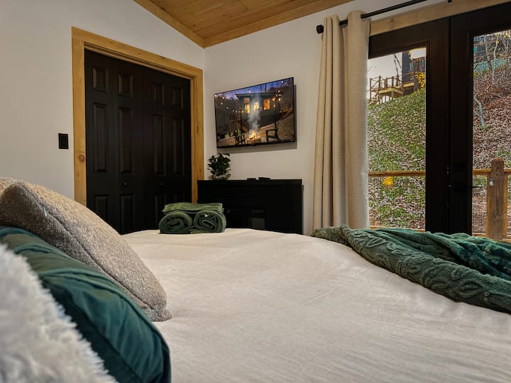 Tento apartmán s manželskou posteľou King je ideálnym miestom na oddych! Vychutnajte si plyšový matrac King a luxusnú posteľnú bielizeň, zatiaľ čo sa pozeráte do lesa a hviezdy veľkými oknami. Táto spálňa má tiež HDTV a elektrický krb na vytvorenie romantického úkrytu. 