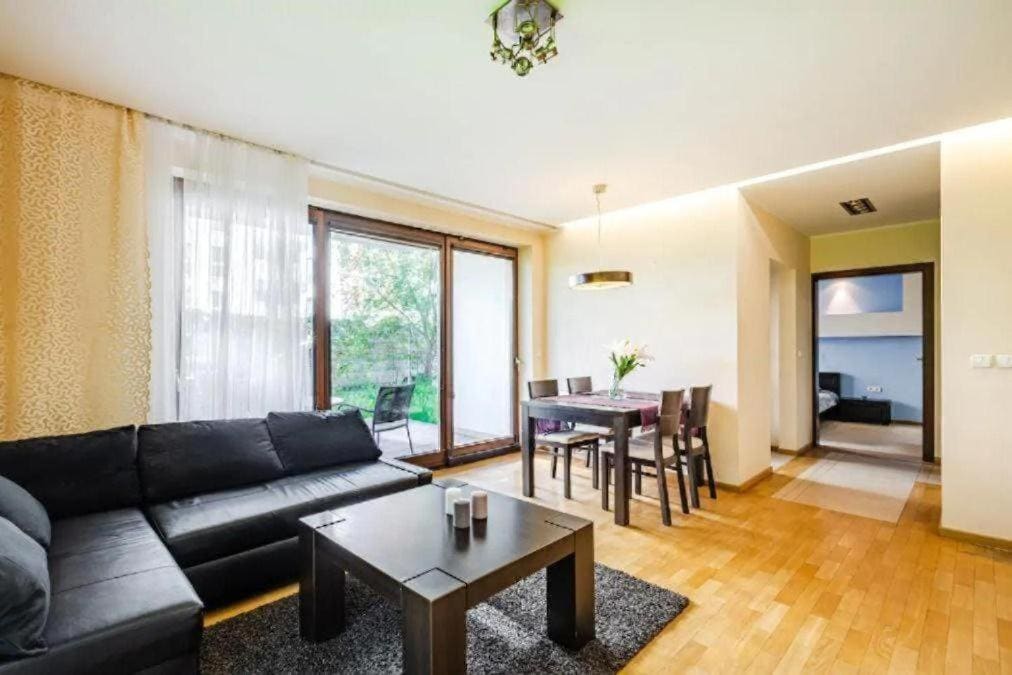 The living area features a dark sectional sofa and a coffee table placed on a textured rug. A dining table with chairs is visible, and large glass doors lead to a terrace, allowing natural light to fill the space. A subtle decorative pendant light hangs above.