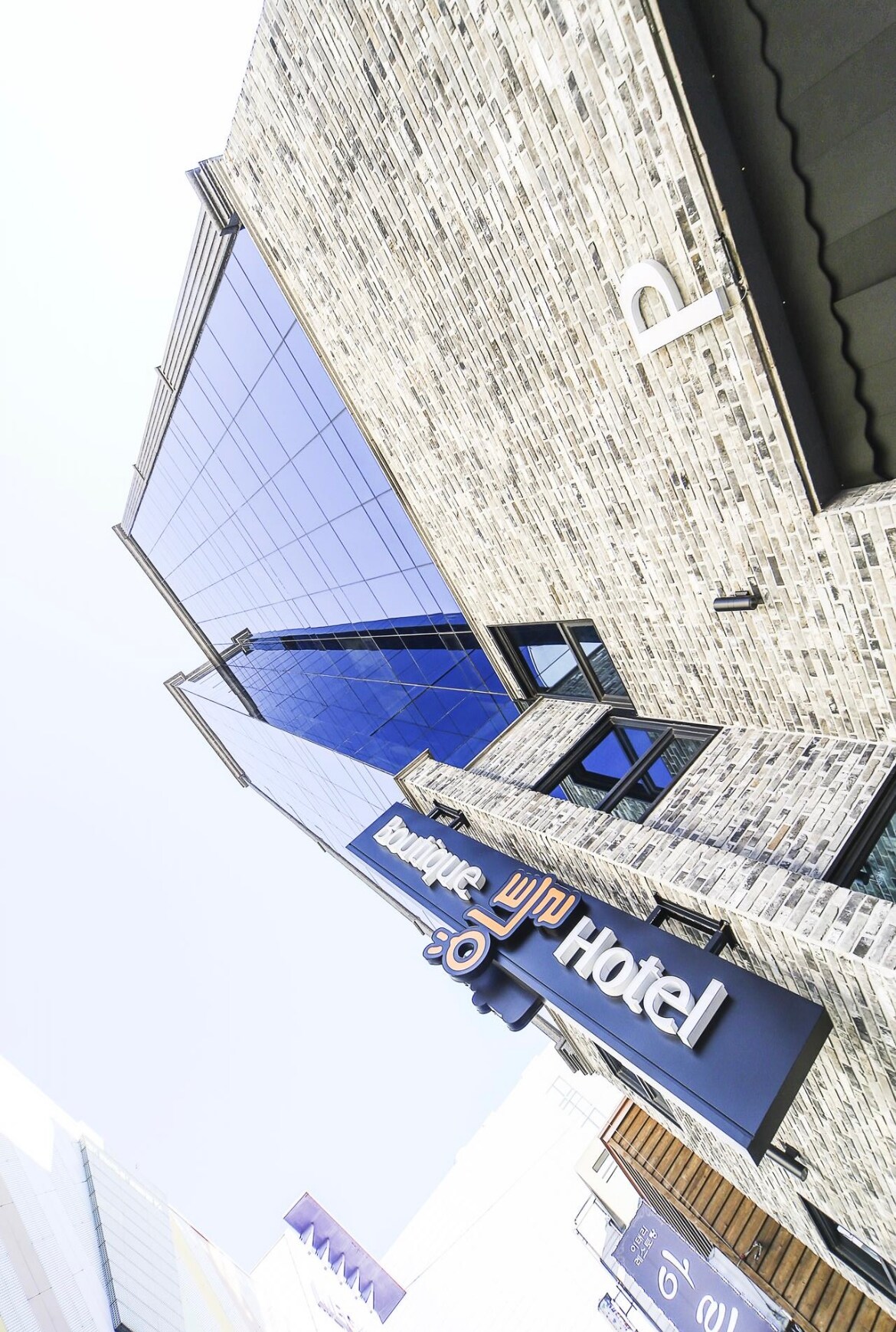 The exterior of the hotel is characterized by a modern design, featuring large glass windows that reflect the sky. The brick facade is complemented by an illuminated sign that displays the hotel name prominently, creating an inviting first impression.