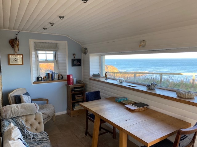 A cozy living area is featured with a wooden table set along a window, offering panoramic sea views. A comfortable armchair and a side table are arranged near the wall, adorned with personal items and decorative touches.