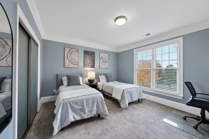 غرفة نوم بسريرين متماثلين وخزانة ملابس وتلفزيون 43بوصة ومساحة عمل مخصصة مع كرسي ومكتب.