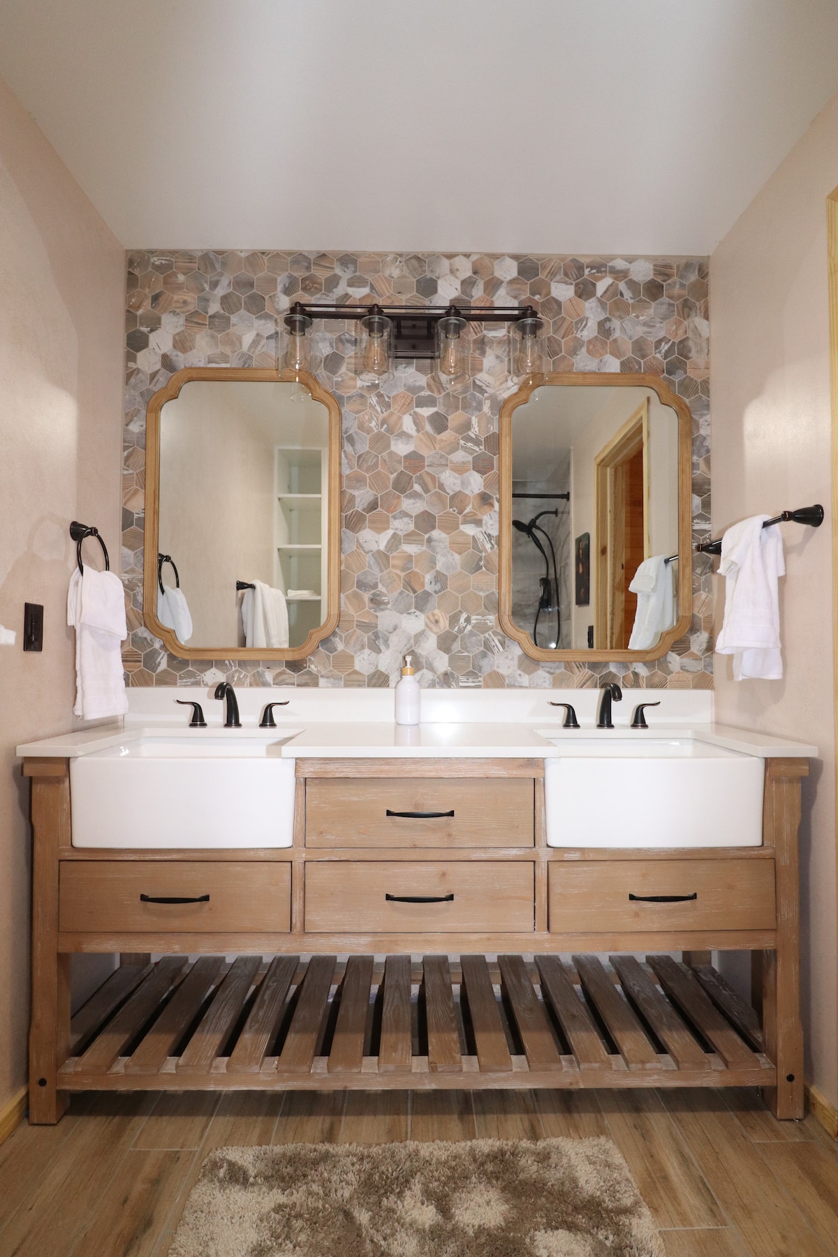 The bathroom features a double vanity with two sinks set in a wooden base. Above each sink, mirrors with decorative frames are mounted on a textured wall of pebbles. Towels hang neatly on fixtures, and natural light illuminates the space.