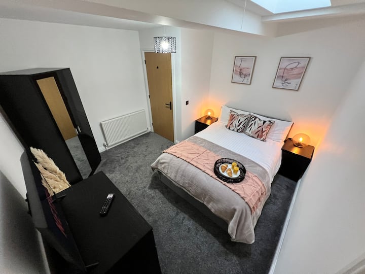 Lichte slaapkamer met een tweepersoonsbed met zacht beddengoed, een handig nachtkastje en een tv voor entertainment wanneer het jou schikt.