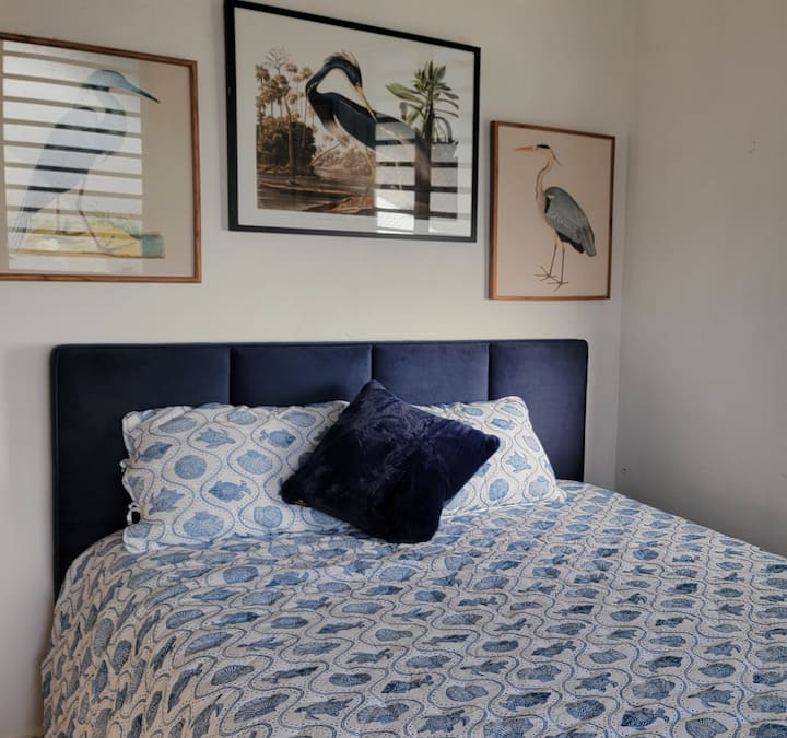 Chumba cha kulala cha kupendeza kilicho na matandiko yaliyohamasishwa na bahari na sanaa ya ndege wa kitropiki, tulivu, na yenye sifa nzuri.