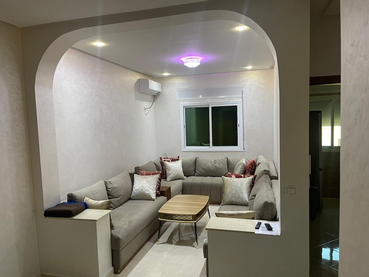 A comfortable seating area is arranged around a low wooden coffee table. Light-colored walls create a bright atmosphere, while a large window allows natural light to enter. Decorative pillows add a touch of color to the sectional sofa, enhancing the inviting setting.