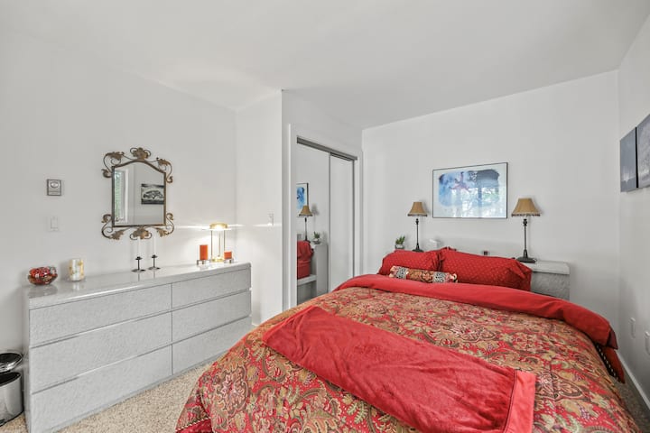 Chambre spacieuse avec un lit queen, des portes de placard avec miroir et une commode, offrant à la fois confort et rangement dans un cadre lumineux et accueillant.