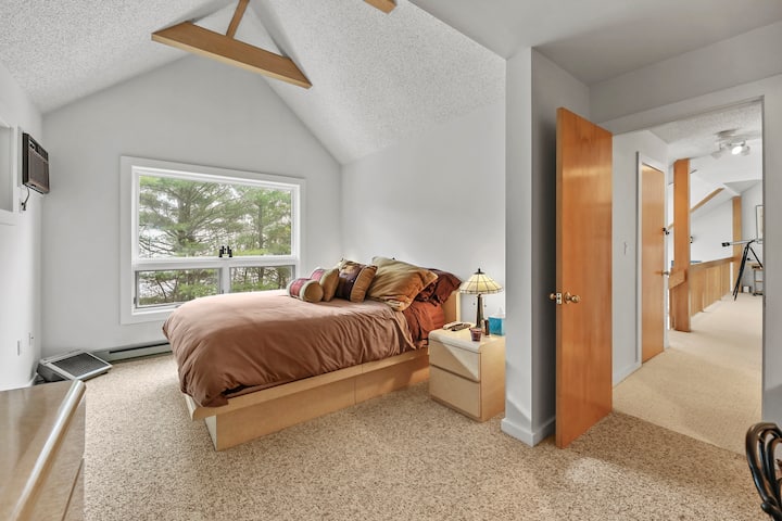 La chambre principale spacieuse est dotée d'un très grand lit et d'une grande baie vitrée qui inonde la pièce de lumière naturelle et offre une vue paisible sur les arbres environnants.