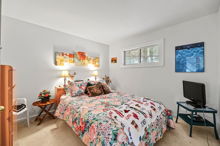 Une chambre lumineuse et accueillante avec un grand lit, une télévision, une décoration charmante et beaucoup de lumière naturelle provenant des fenêtres d'angle.