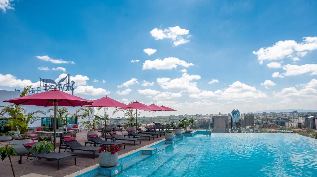 An infinity pool is showcased on a rooftop terrace, surrounded by lounge chairs with pink umbrellas. The panoramic view of Nairobi's skyline is visible against a bright blue sky dotted with white clouds.