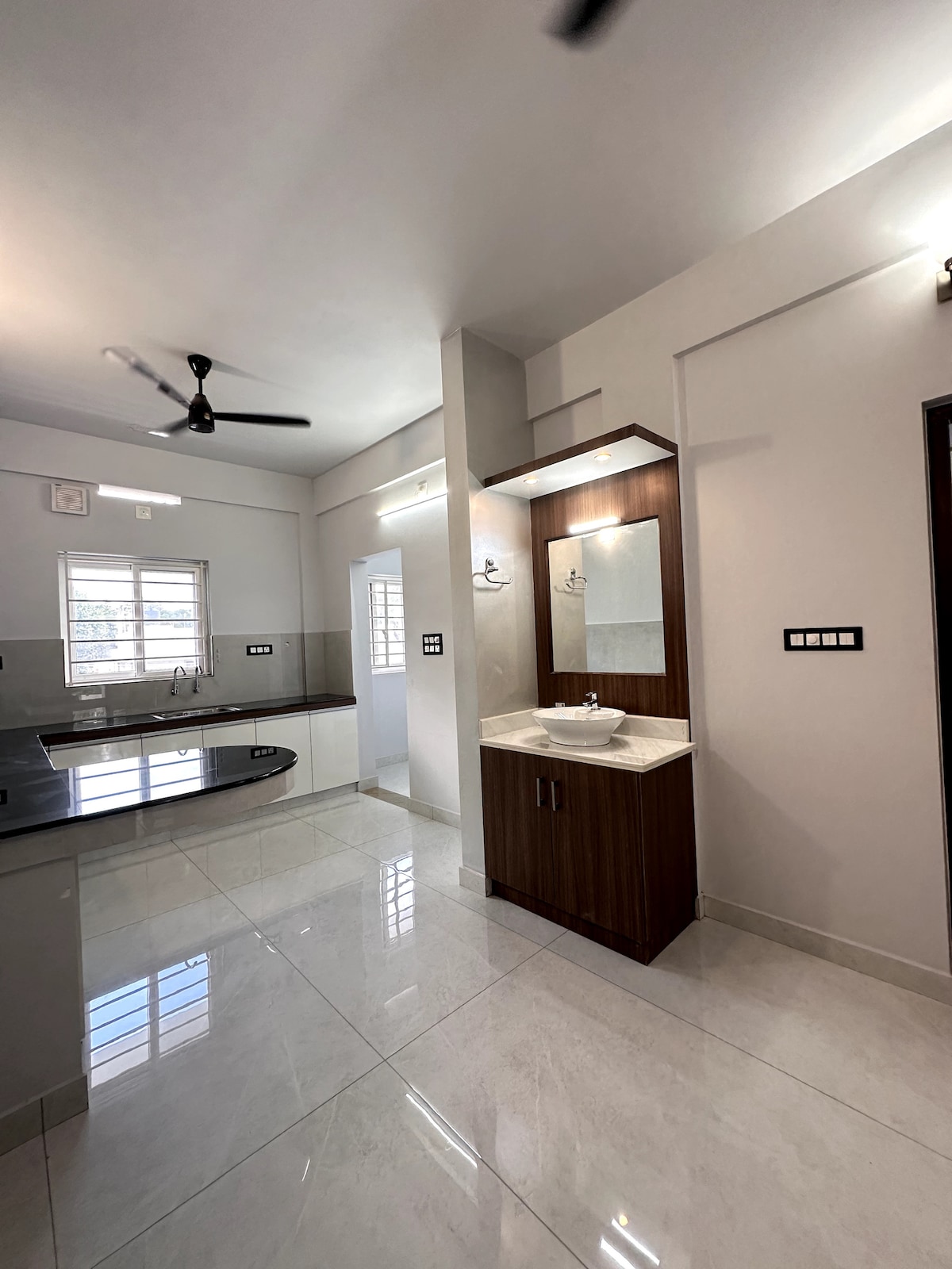 The kitchen showcases modern cabinetry and a granite countertop, paired with a stylish sink. Natural light filters through a window, illuminating the tiled floor. A mirror and basin are integrated into a cabinet, adding functionality to the space.