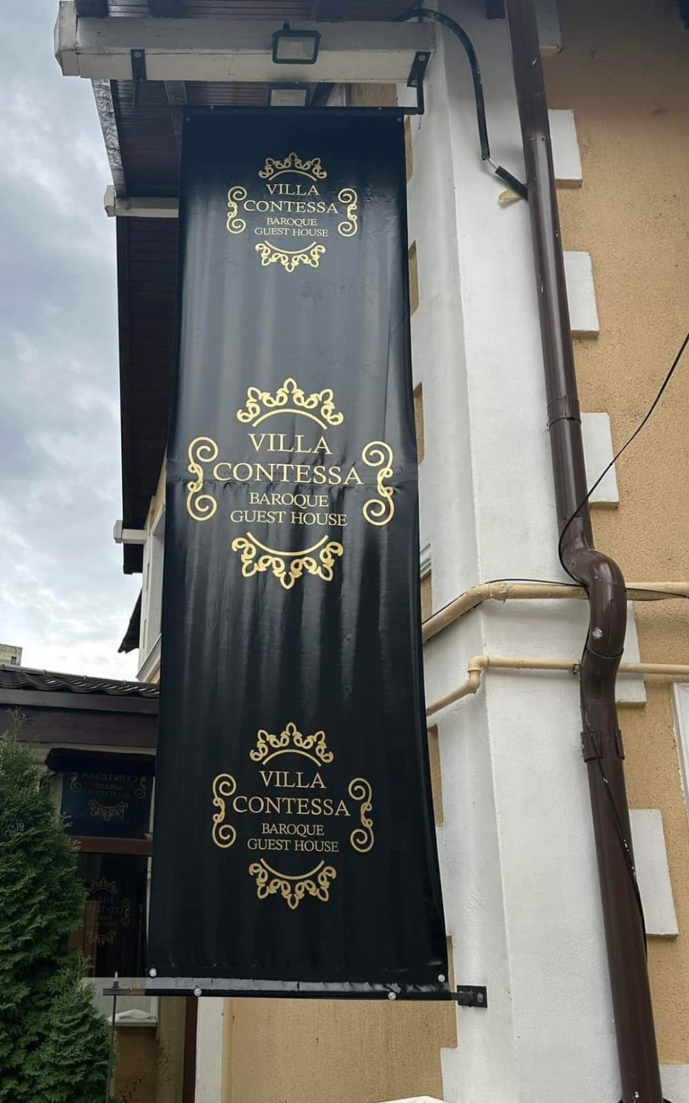 A large banner displays the name "Villa Contessa" in elegant gold lettering against a black background. The banner indicates the establishment’s focus on Baroque style and is hung from the exterior of the building, highlighting its prominence.