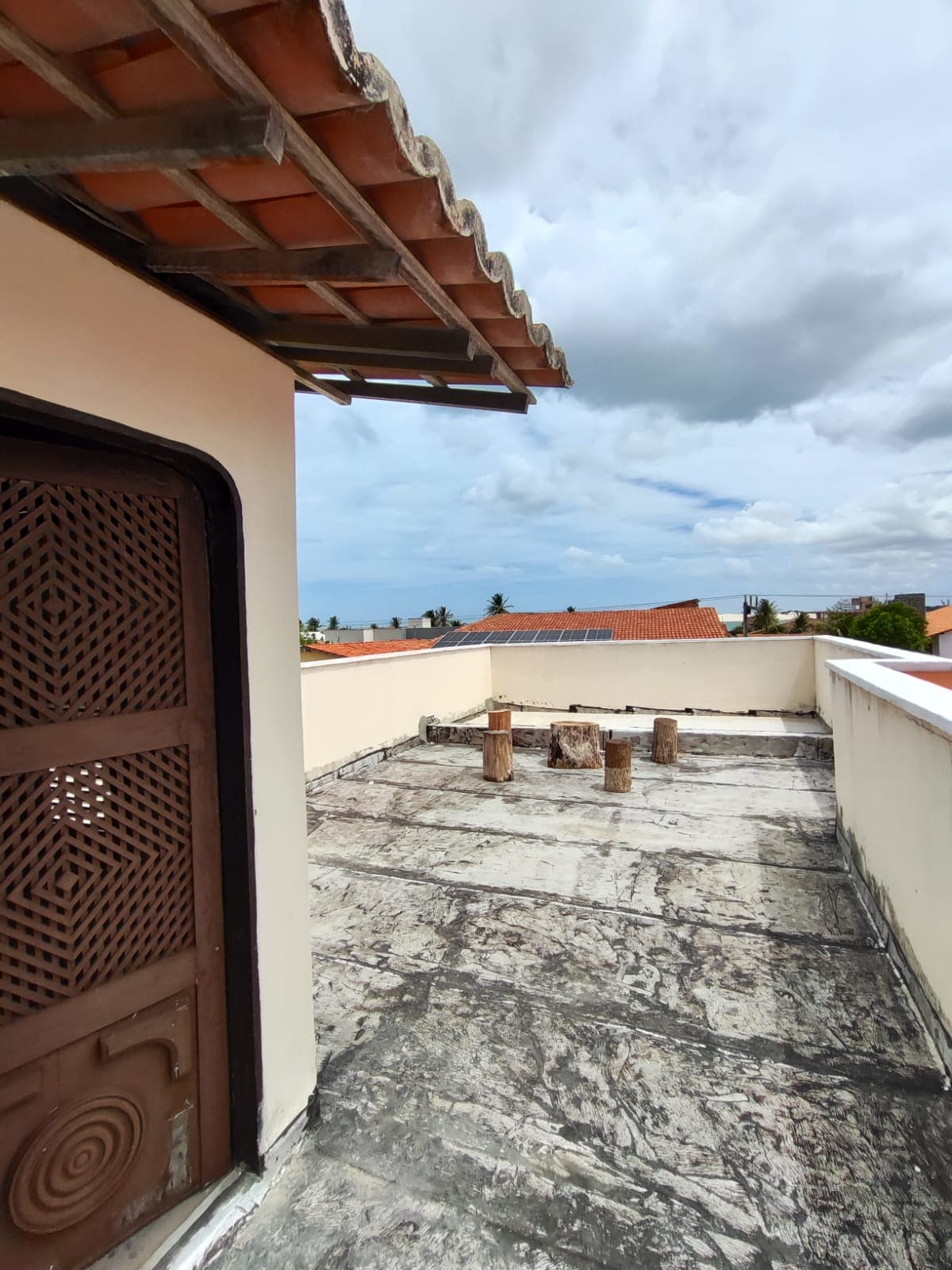 The rooftop area features a textured surface with several wooden posts positioned throughout. A view of the surrounding rooftops is visible under a partly cloudy sky, offering an open and unobstructed space for outdoor experiences.