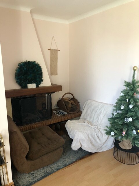 A cozy seating area is presented, featuring a soft armchair draped with a light blanket. A rustic wooden bench accommodates decorative items near a fireplace, while a small, tastefully decorated Christmas tree adds a festive touch to the corner.