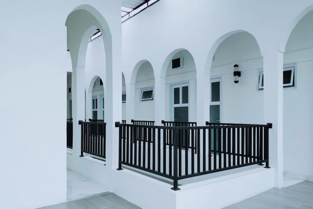 A series of elegant white arches frame the balcony area, featuring a black railing that enhances the architectural design. Natural light is invited through the windows, creating a bright atmosphere in the spacious corridor.