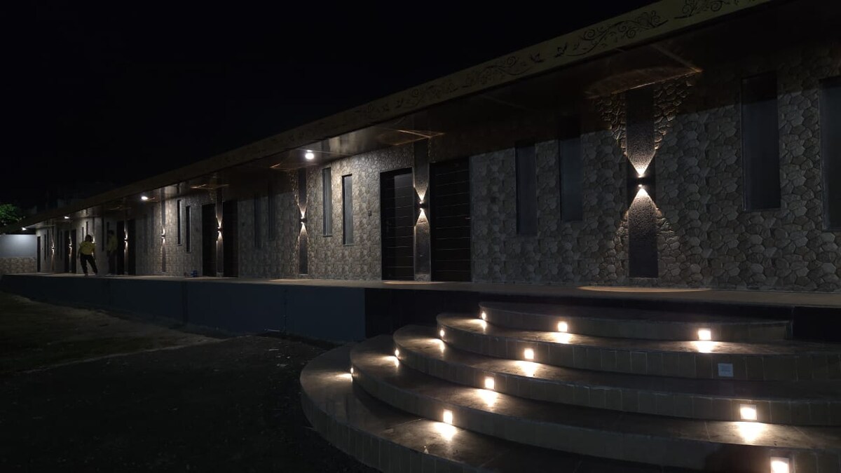 The exterior of the property is displayed at night, featuring a unique stone facade illuminated by strategically placed outdoor lighting. Stairs lead to an entrance, with soft lighting creating a welcoming pathway alongside the building.