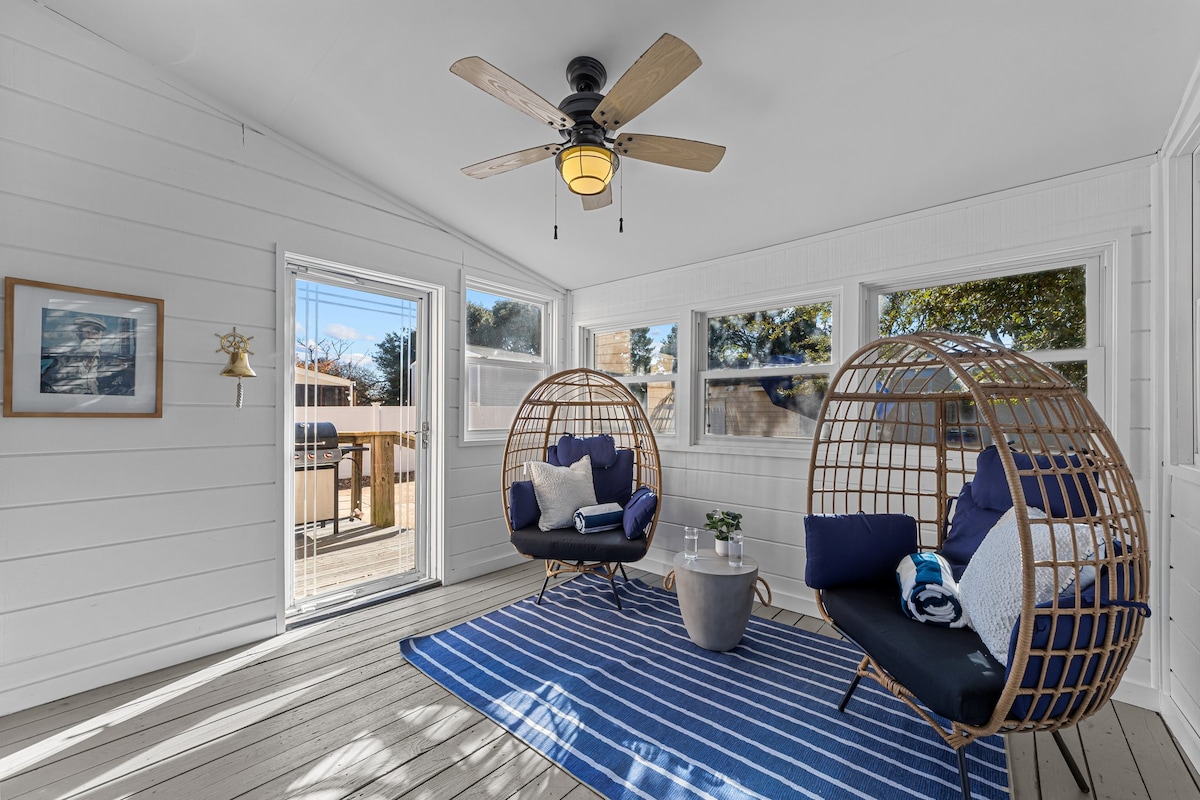 The sun room features unique egg chairs providing comfortable seating. A ceiling fan is positioned overhead to enhance airflow. Large windows allow natural light to brighten the space, complemented by a patterned area rug on the floor.