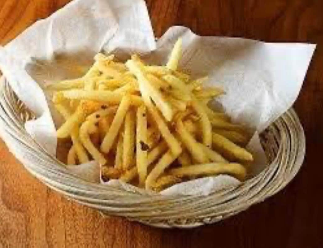 A woven basket is presented, holding a generous serving of golden fries. The fries are arranged in a casual pile, resting on a piece of parchment paper. The wooden surface beneath adds a warm tone to the overall presentation.