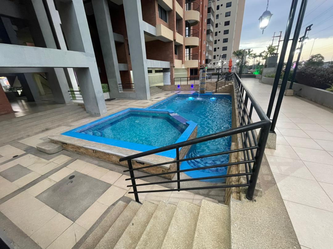 A well-maintained swimming pool area features a rectangular pool complemented by a smaller hexagonal pool. Both are surrounded by a smooth stone deck and steel railings, providing access to the water. Soft blue lights illuminate the pools, enhancing the calming environment.