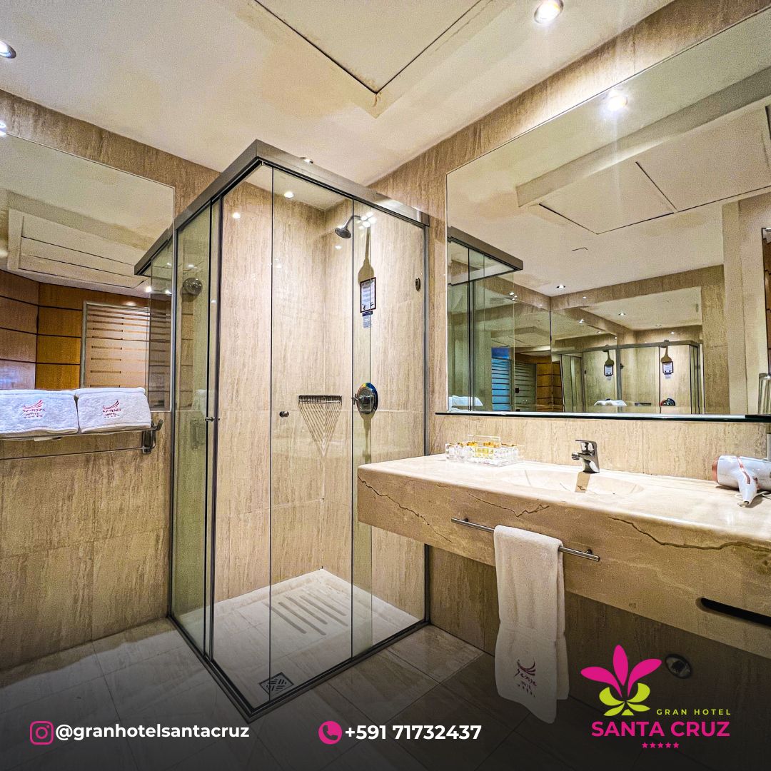 A modern bathroom is equipped with a spacious glass shower enclosure and a stone vanity. The sink features a sleek faucet, and a large mirror is mounted above the counter, enhancing the room's bright ambiance. Soft towels are neatly arranged nearby.
