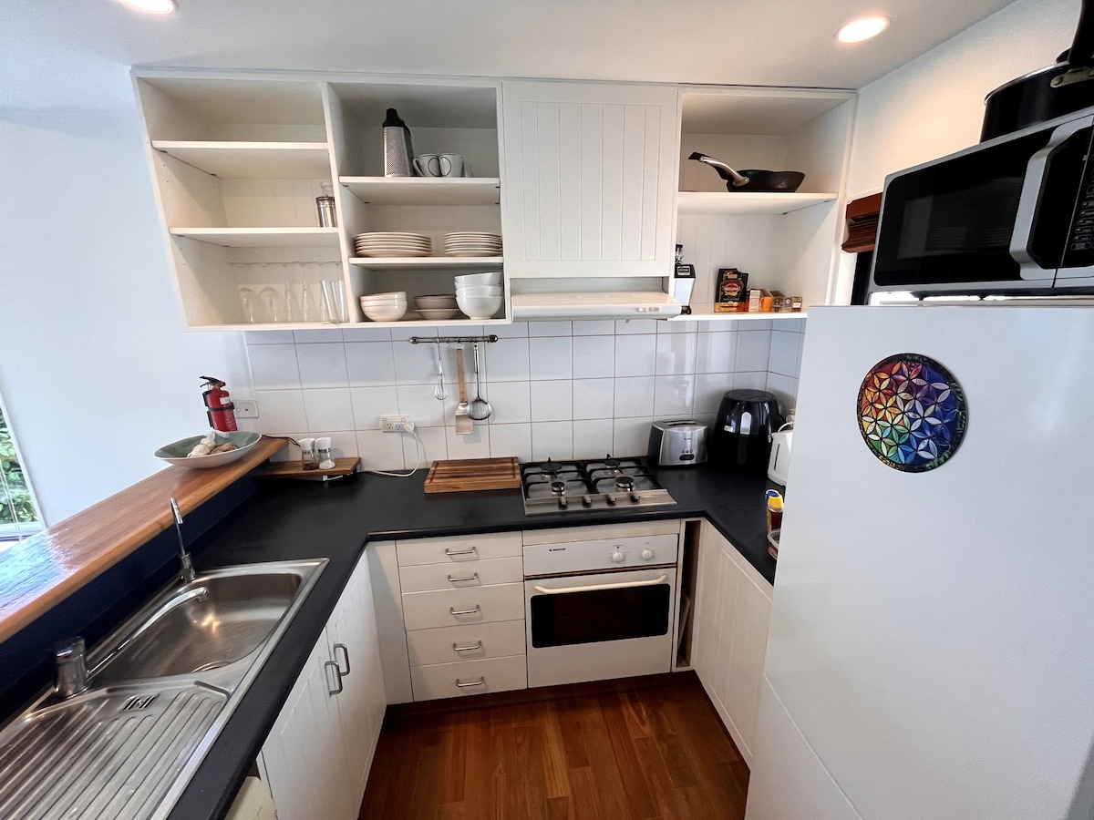 The kitchen features modern appliances, including a microwave and a stove. White cabinetry provides ample storage, while counter space allows for meal preparation. A sink is positioned next to a window, offering natural light. Cookware and utensils are neatly organized on shelves.