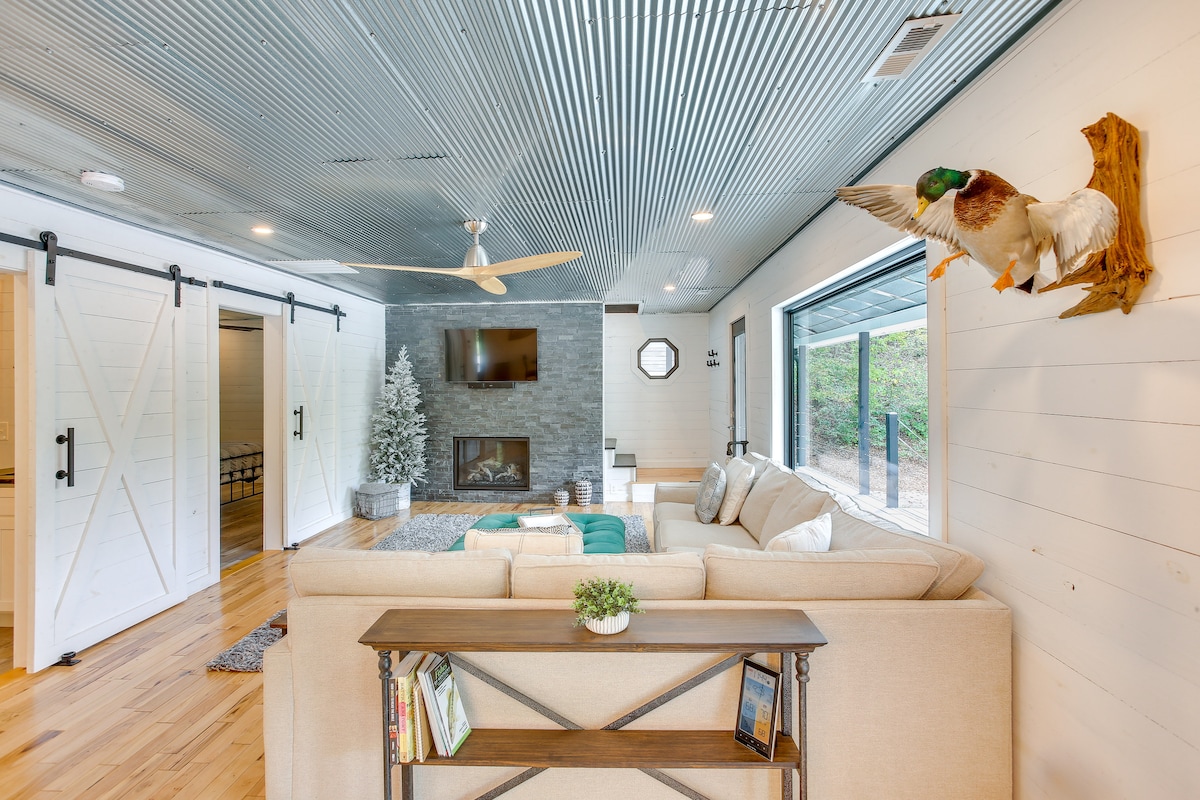 A spacious living area features a comfortable beige sofa and a stylish coffee table. A modern gas fireplace and a mounted television create a cozy ambiance. A decorative taxidermy duck is displayed on the wall, while sliding barn doors lead to private rooms.